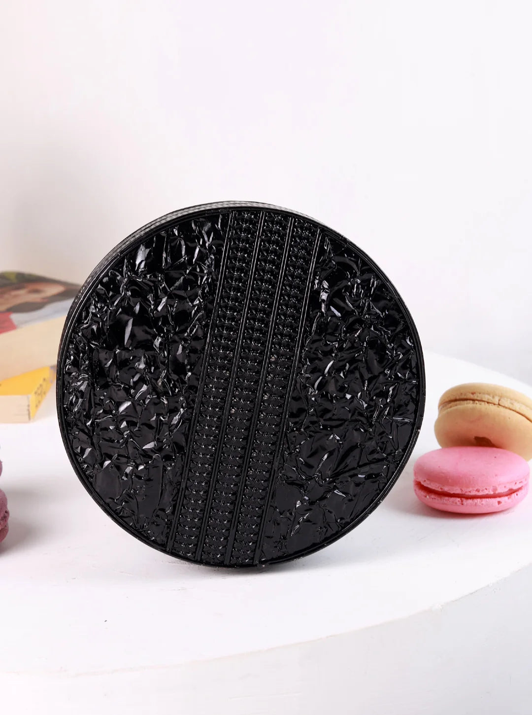 Black textured round object on a white surface with colorful items in the background