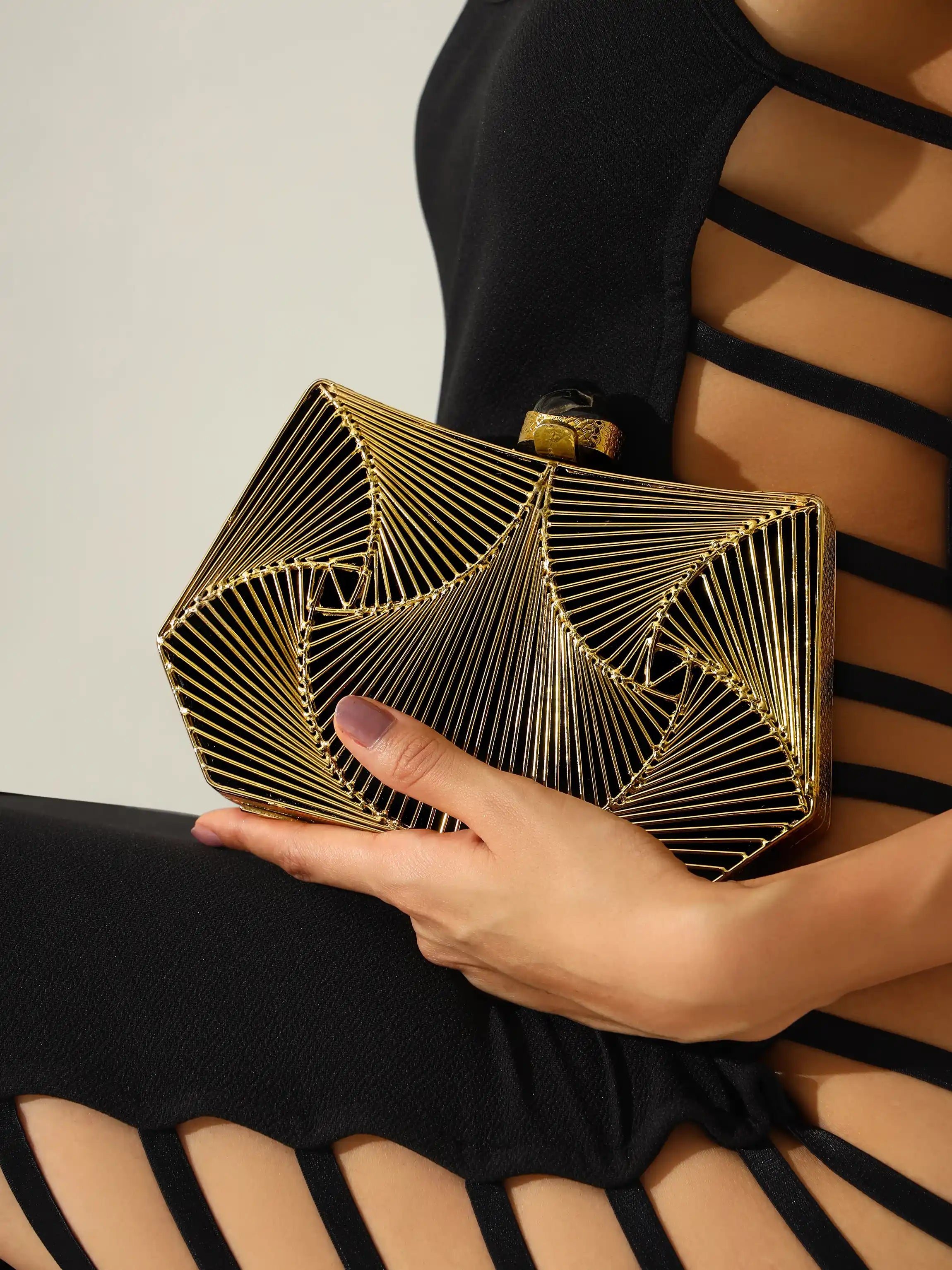 Gold geometric clutch held by a hand against a neutral background