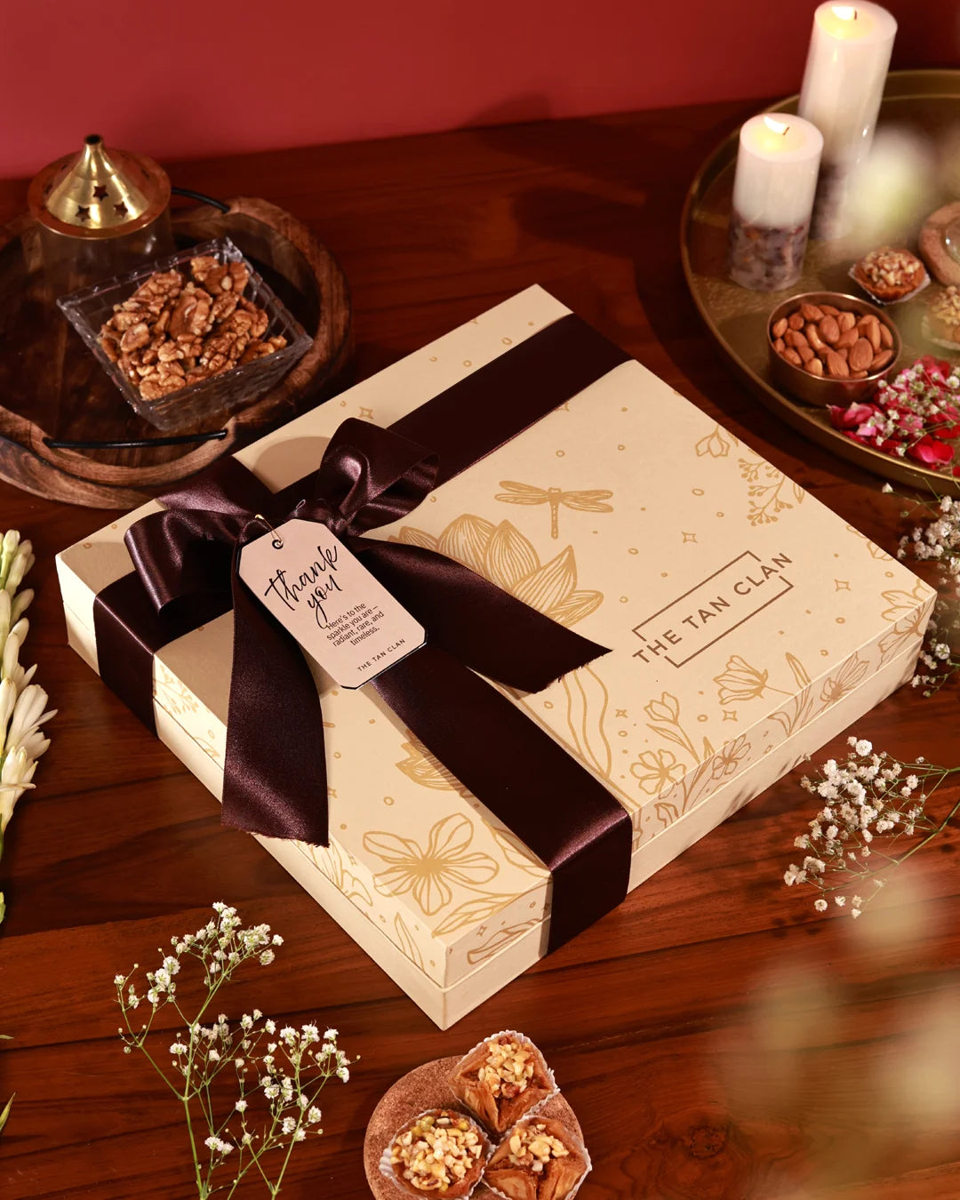 Gift box with a decorative ribbon and tag on a wooden surface with candles and snacks.