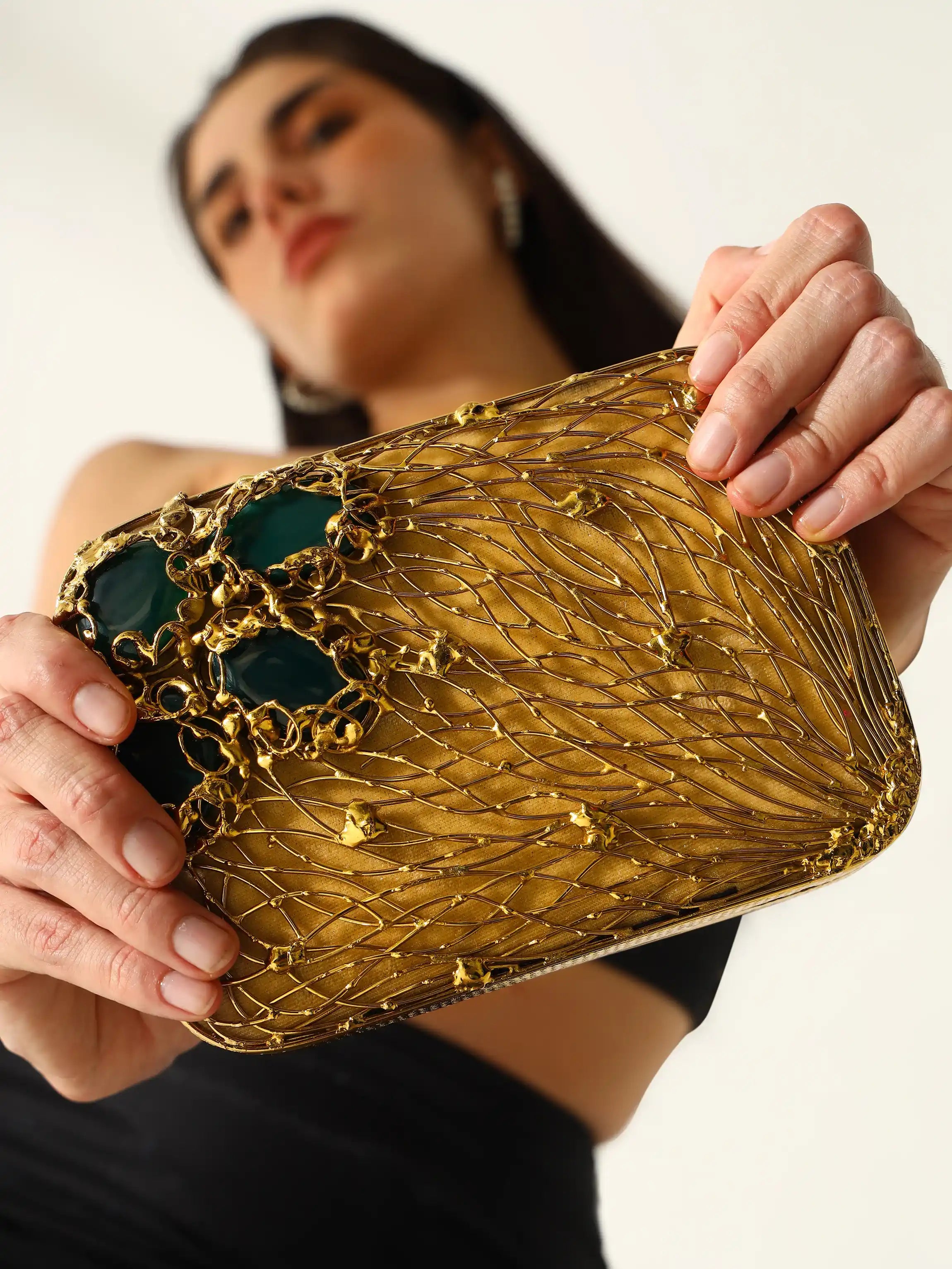 Woman holding a gold clutch with intricate design