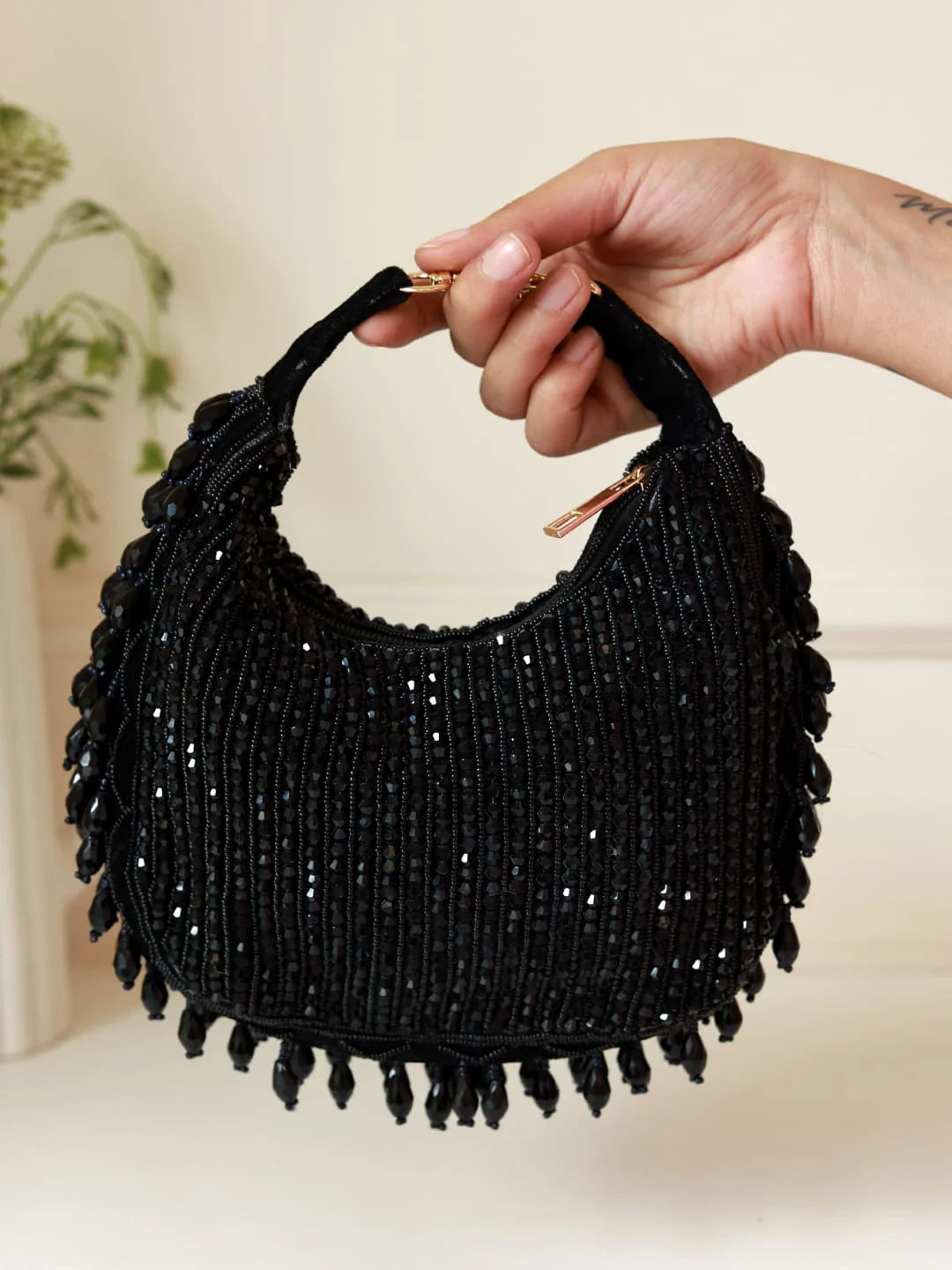 Black beaded handbag held by a hand against a neutral background