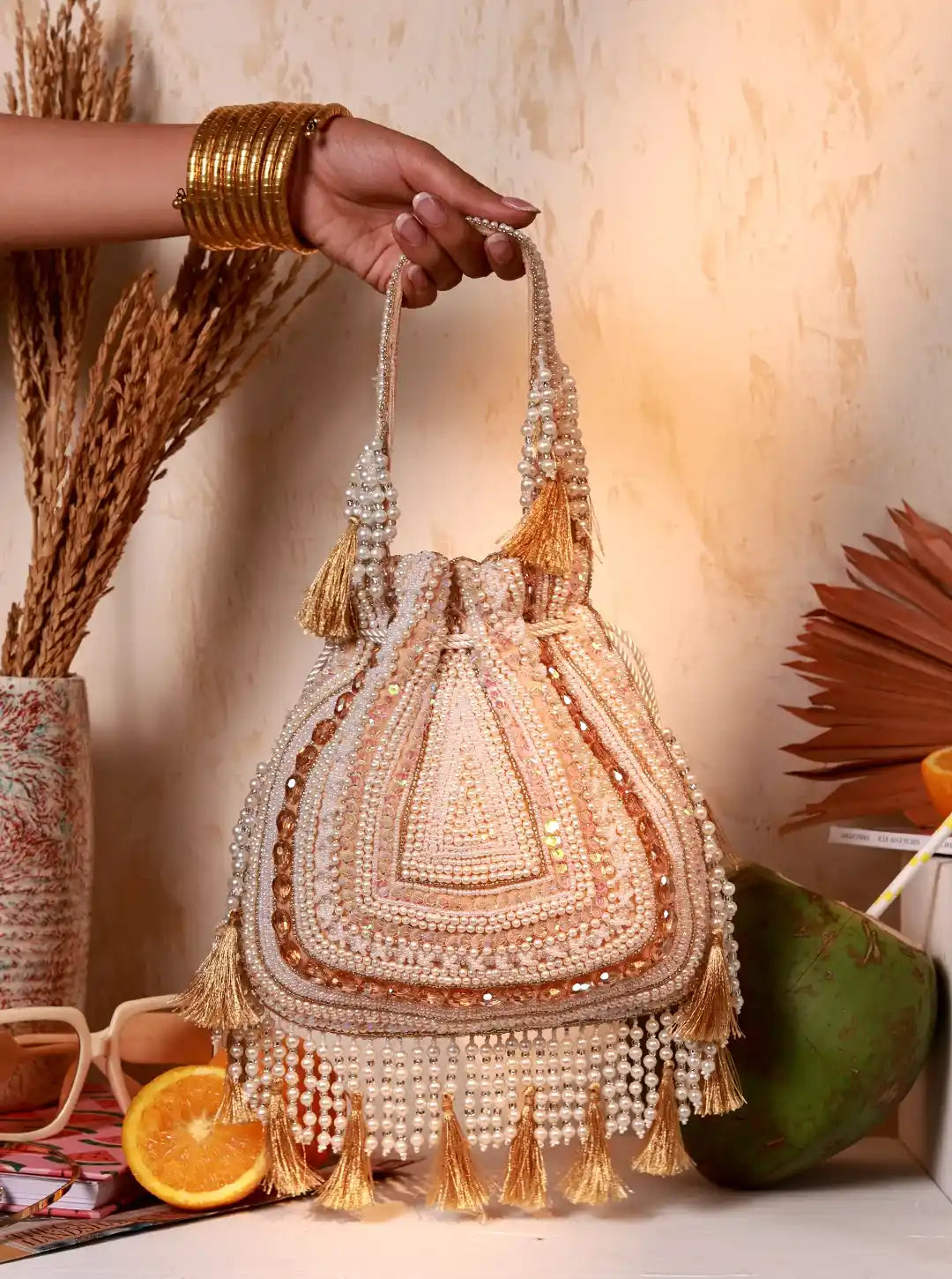 Hand holding a beaded handbag with tassels against a warm-toned background