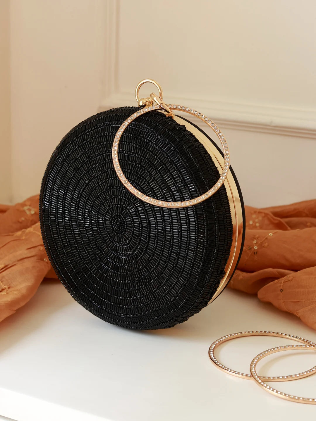 Black woven handbag with gold circular handles on a white surface with orange fabric in the background