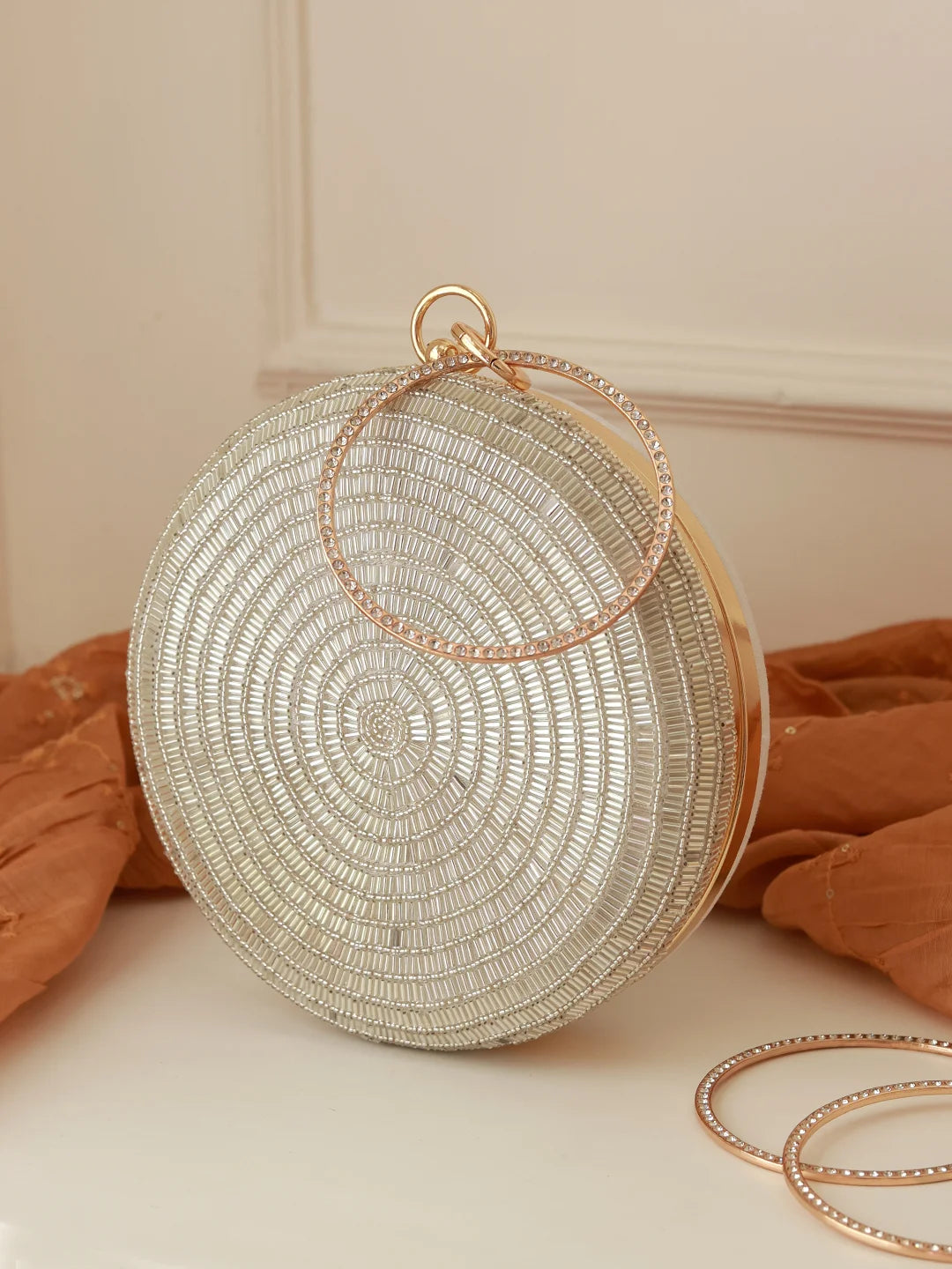 Round beaded clutch bag with gold handle on a neutral background