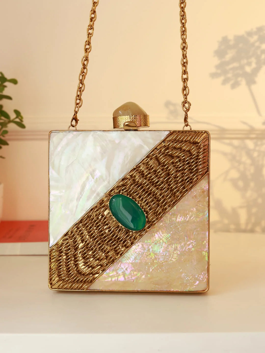 Square handbag with gold chain, green stone, and iridescent material on a neutral background