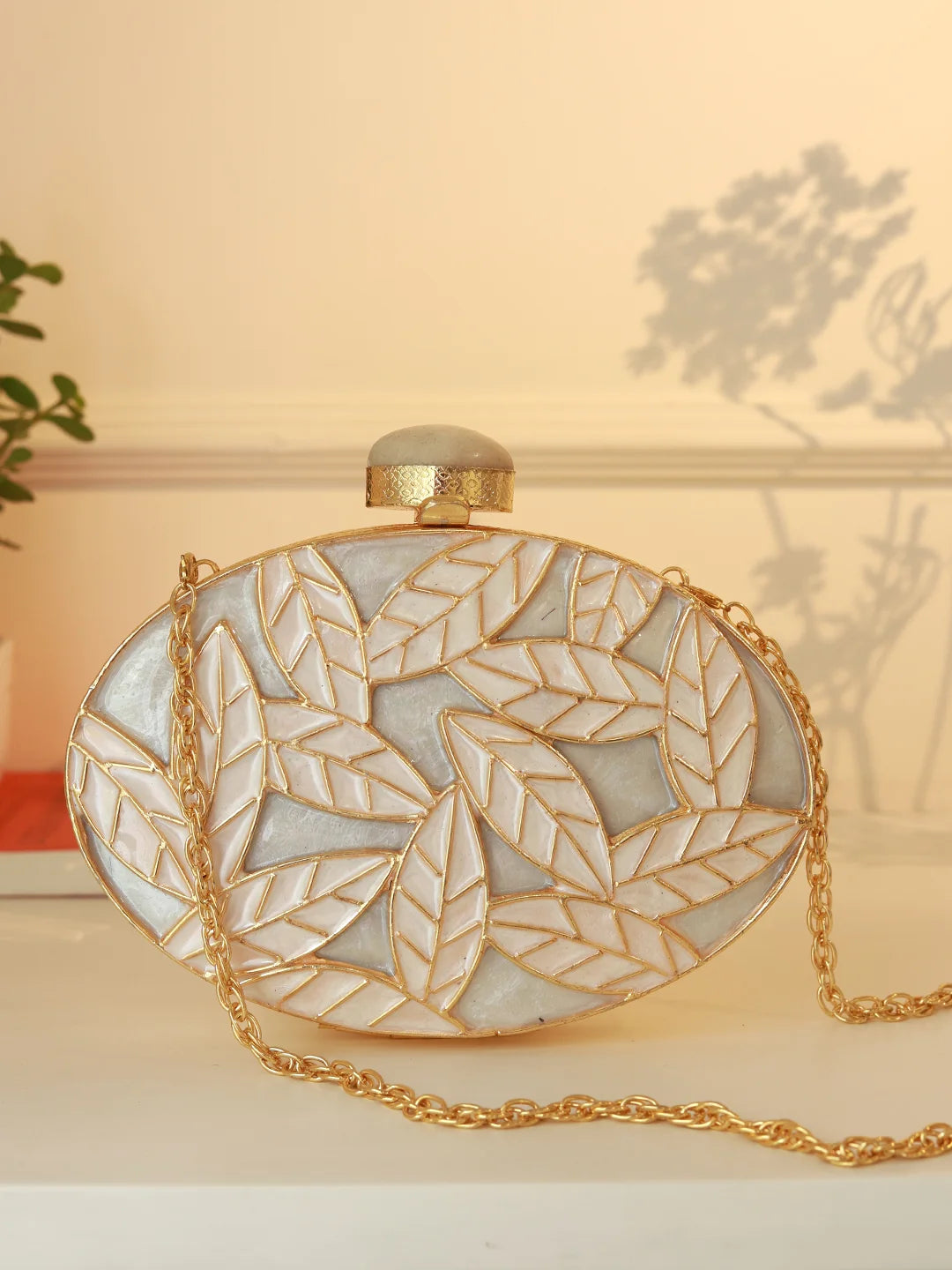Elegant clutch bag with leaf pattern and gold chain on a neutral background