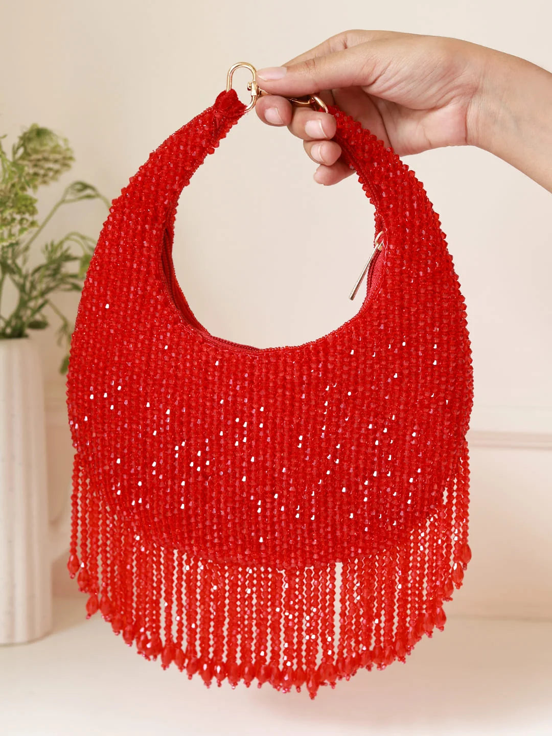 Red beaded handbag with fringe held by a hand against a neutral background