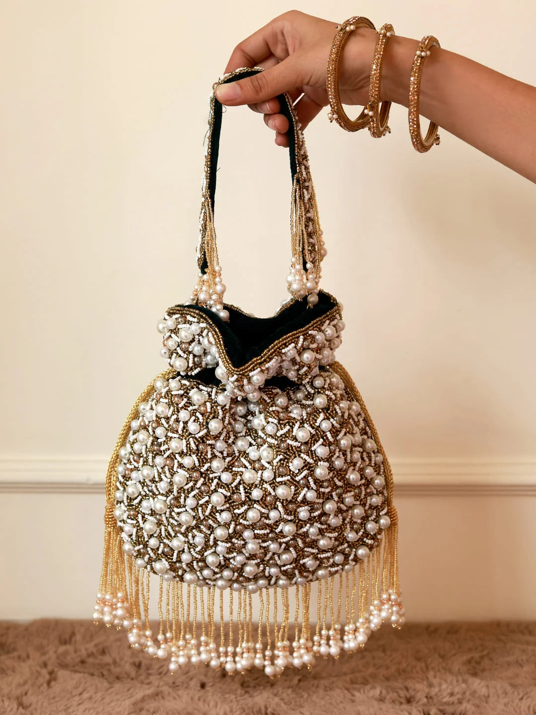 Handbag with pearl embellishments held by a hand against a neutral background