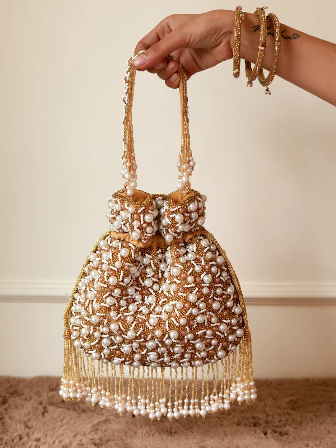 Handbag with pearl detailing held by a hand against a neutral background