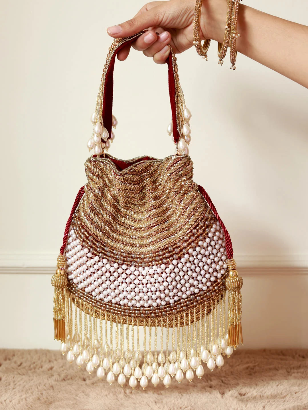 Handbag with beaded details held by a hand against a neutral background