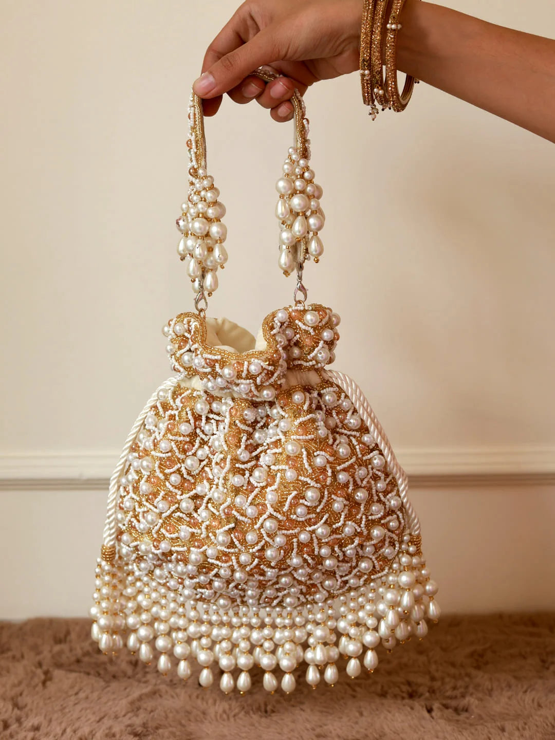 Handbag with pearl embellishments held by a hand against a neutral background