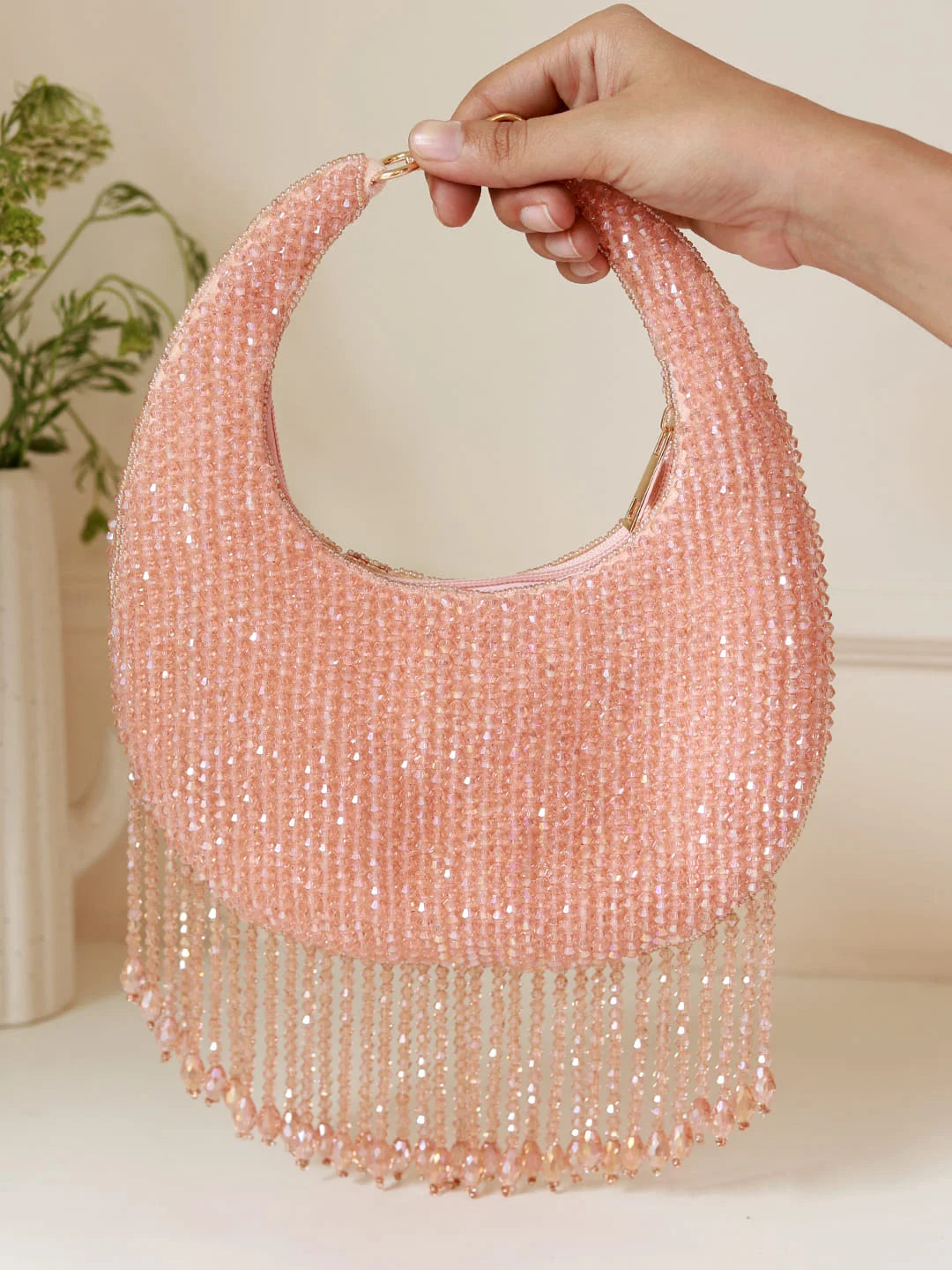 Pink beaded handbag with fringe held by a hand against a neutral background