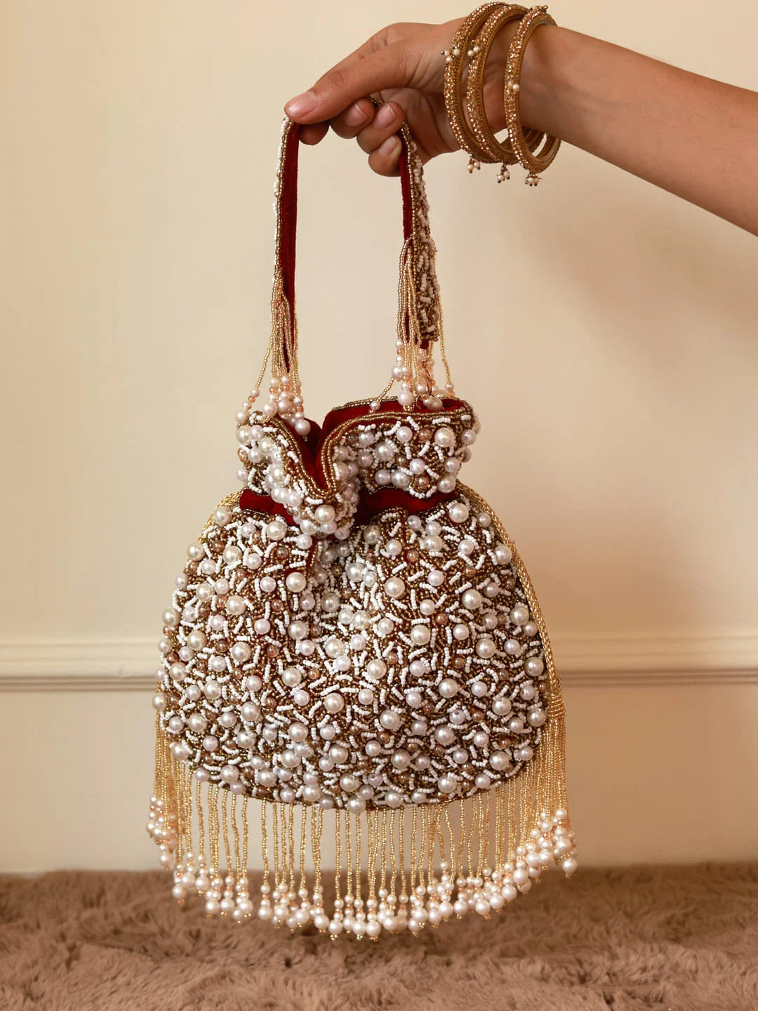 Decorative handbag with pearl embellishments held by a hand against a neutral background