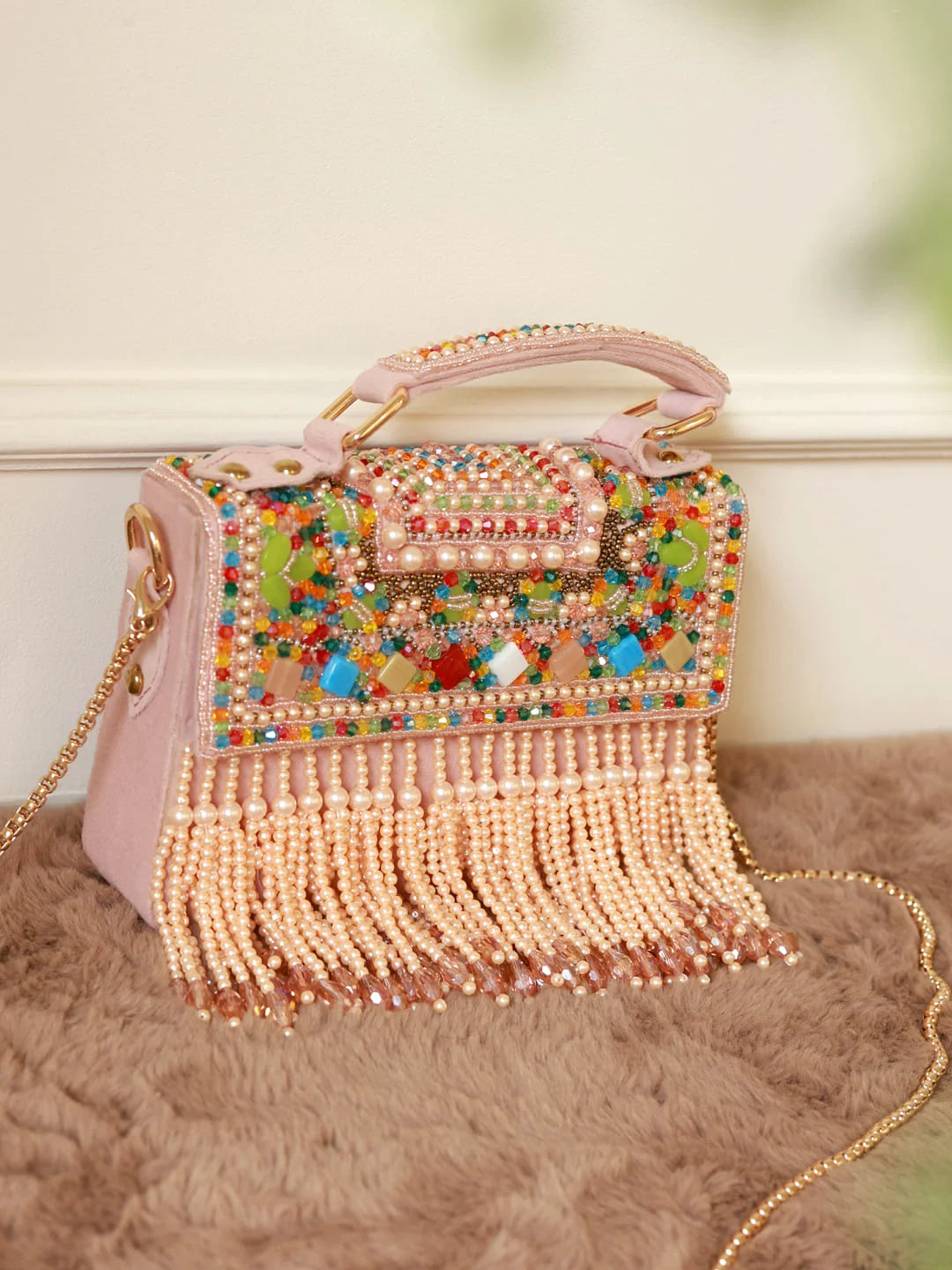 Decorative handbag with colorful beaded design and fringes on a soft surface.