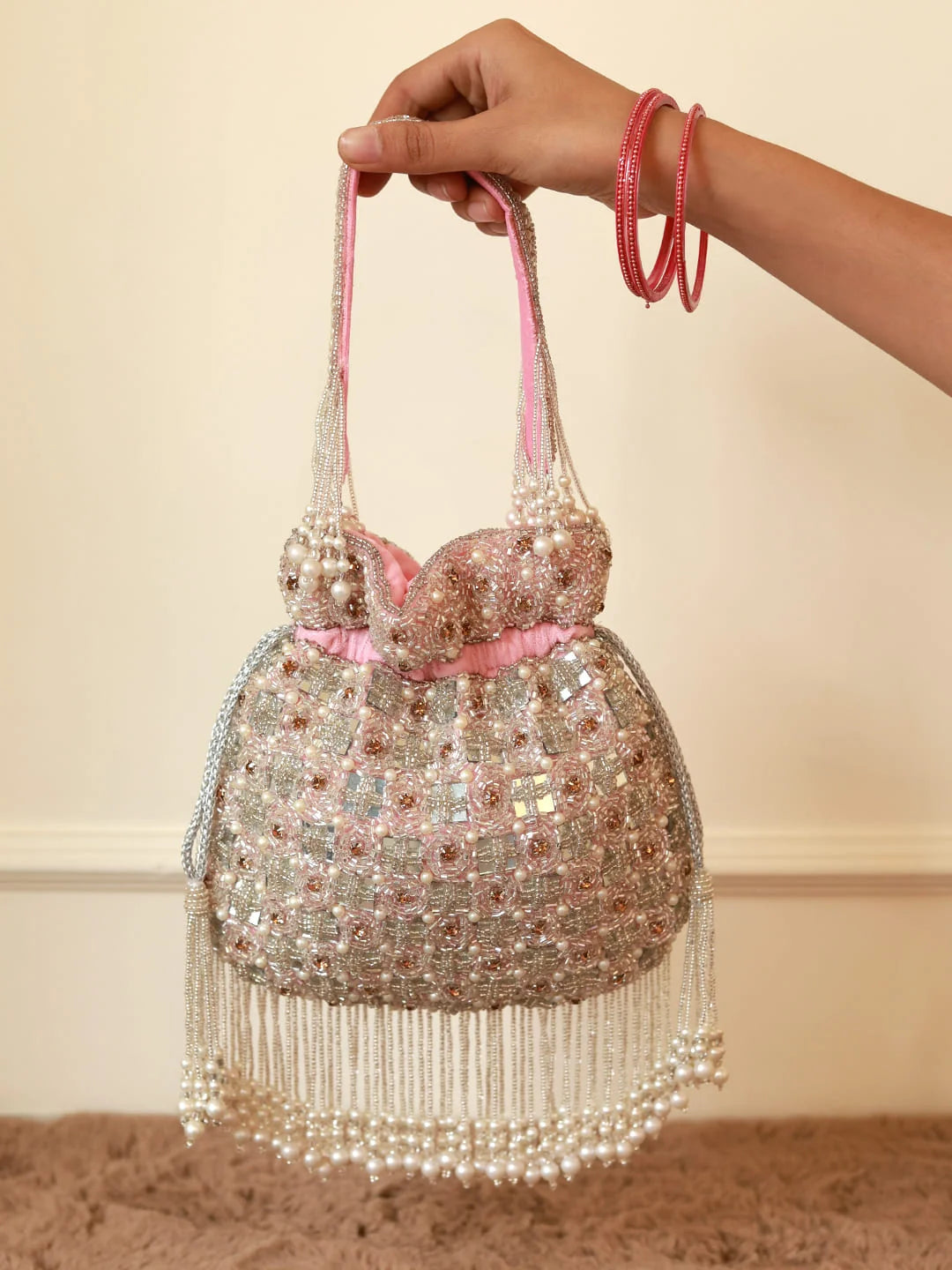 Hand holding a beaded handbag with pink accents against a neutral background