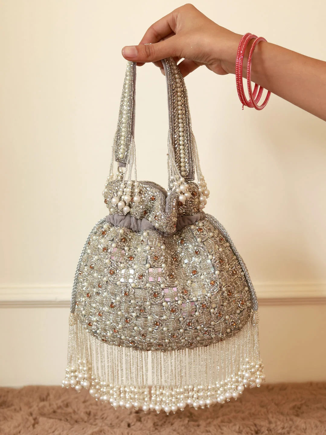 Hand holding a beaded handbag with a plain background