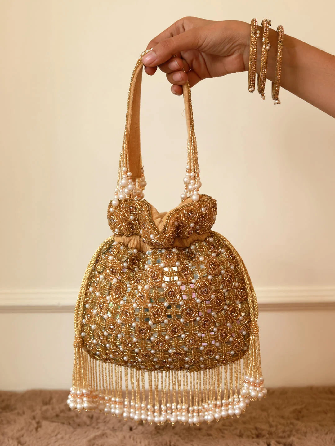 Gold beaded handbag with tassels held by a hand against a neutral background