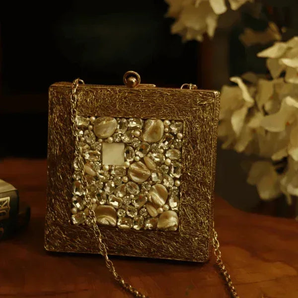A brass clutch purse with intricate embellishments and decorative details, designed by The Tan Clan.