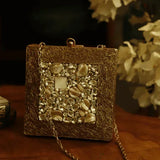 A brass clutch purse with intricate embellishments and decorative details, designed by The Tan Clan.