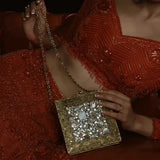 A brass clutch bag with intricate embellishments, featuring a stylish design by The Tan Clan.
