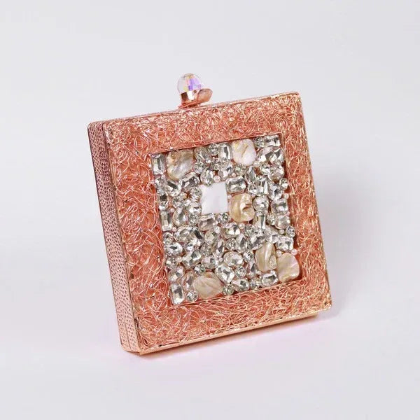A brass clutch with intricate embellishments from The Tan Clan, featuring detailed decorative patterns and a sleek, elegant design.