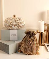 A gold Swarn mini lotus potli and white Elizah Zardozi clutch with intricate embroidery, styled together for elegant occasions.