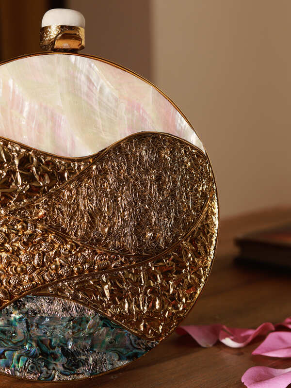 Crescent-shaped round clutch bag with shimmering mother of pearl surface by The Tan Clan, featuring a sleek elegant design.