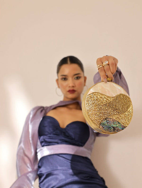 Crescent-shaped mother of pearl clutch bag by The Tan Clan with a glossy, iridescent surface and elegant design.