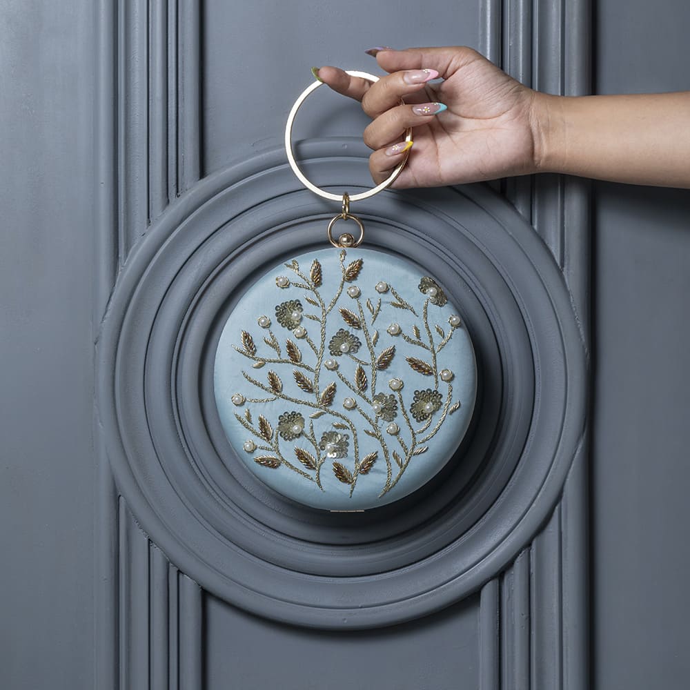Blue round clutch purse with intricate hand embroidery, crafted by The Tan Clan, featuring a stylish and colorful design.