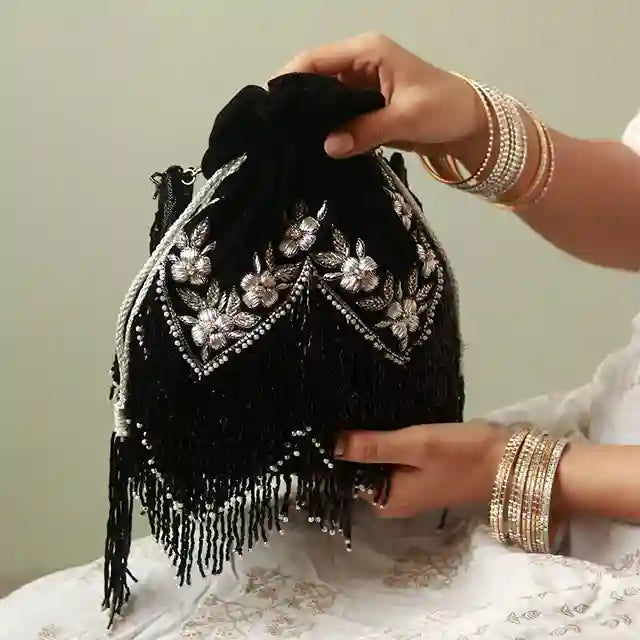 Black tassel potli bag with handle from The Tan Clan, featuring intricate embroidery and a drawstring closure.