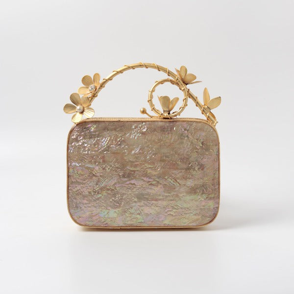 Naira mother of pearl clutch with brass embellished handle by The Tan Clan, showcasing elegant pearlescent surface and detailed hardware.