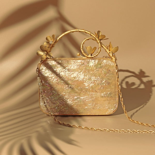 Naira Mother of Pearl clutch by The Tan Clan with brass embellished handle, featuring a shimmering pearl surface and elegant design.