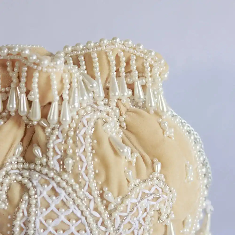 Beige Sukoon hand-embroidered potli bag with pearl handle from The Tan Clan, showcasing intricate embroidery and elegant design.