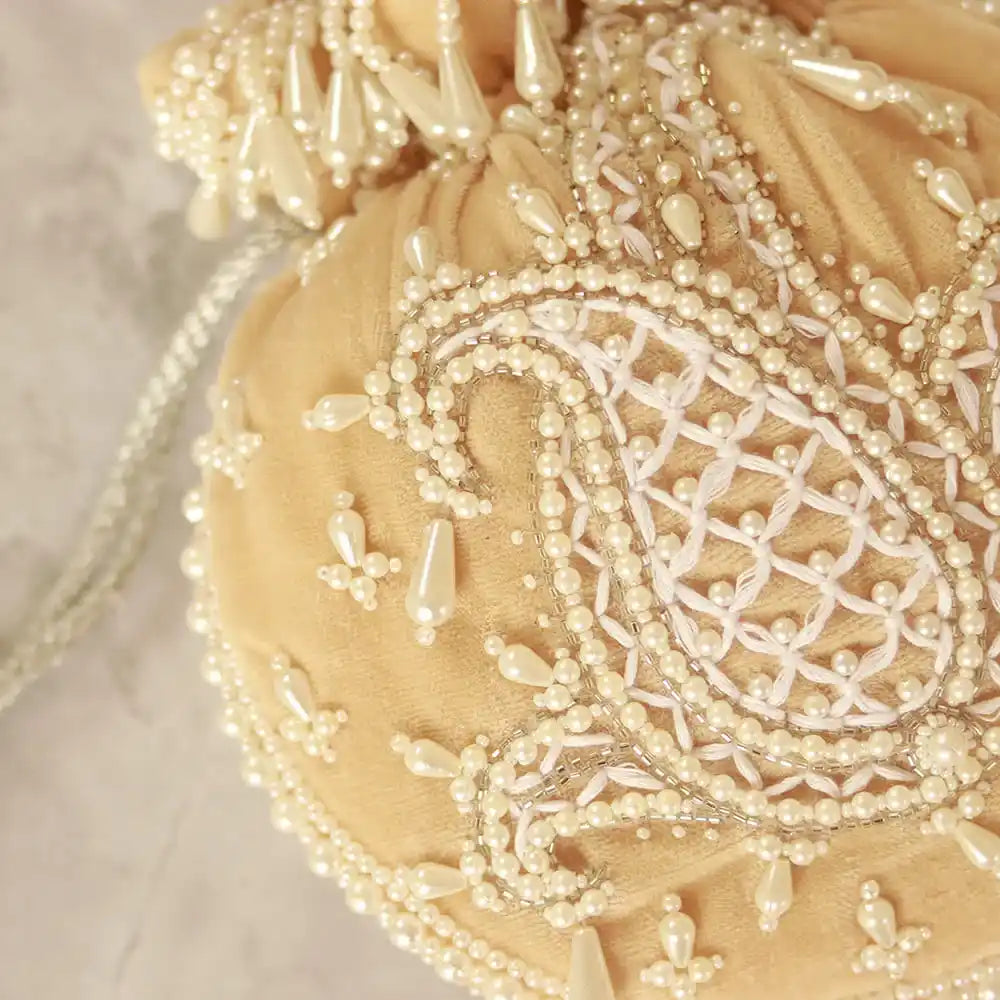Beige Sukoon hand-embroidered potli bag with pearl handle from The Tan Clan, featuring intricate embroidery and elegant design.