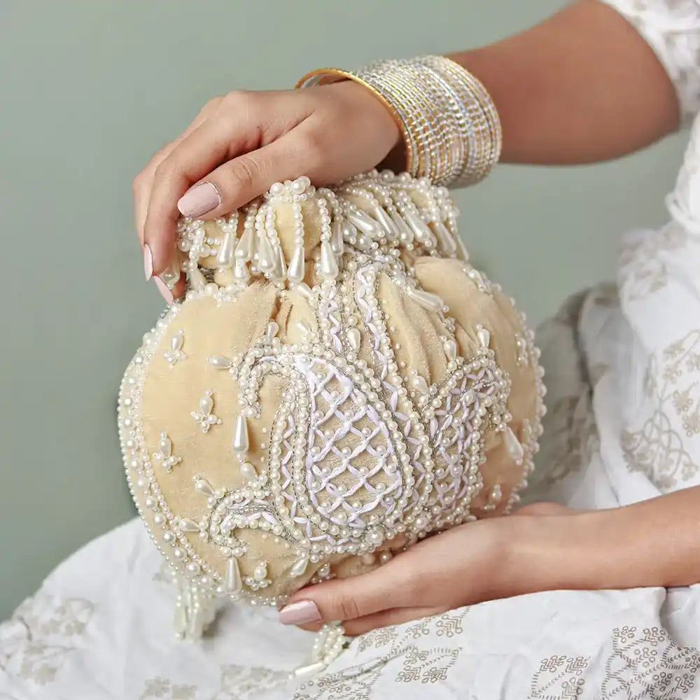 Beige Sukoon hand-embroidered potli bag with pearl handle, crafted by The Tan Clan, featuring intricate embroidery and elegant design.