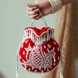Red Sukoon hand-embroidered potli bag with pearl handle by The Tan Clan, featuring intricate embroidery and elegant design.