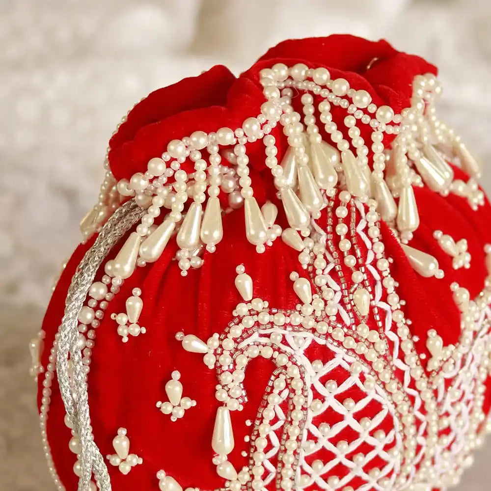Red Sukoon hand-embroidered potli bag with pearl handle from The Tan Clan, showcasing intricate embroidery and elegant design.