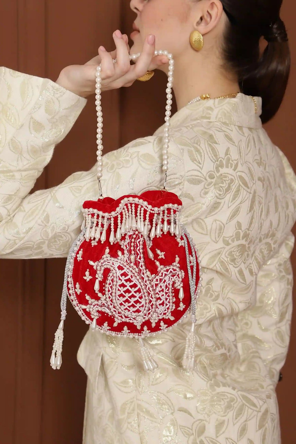 Red Sukoon hand-embroidered potli bag with pearl handle by The Tan Clan, featuring intricate embroidery and elegant design.