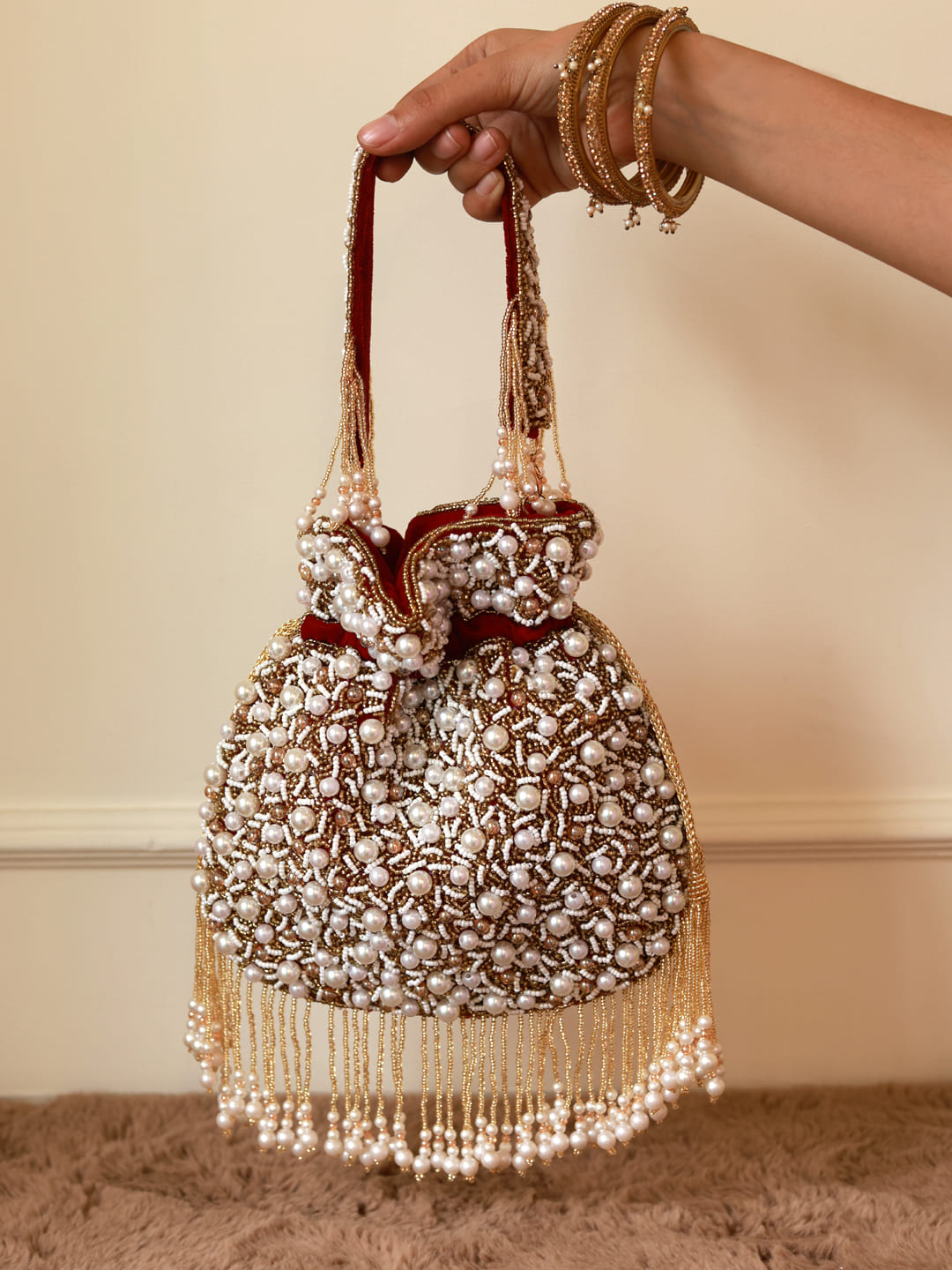 Red pearl potli bag with tassels from The Tan Clan, featuring intricate design and traditional Indian style.